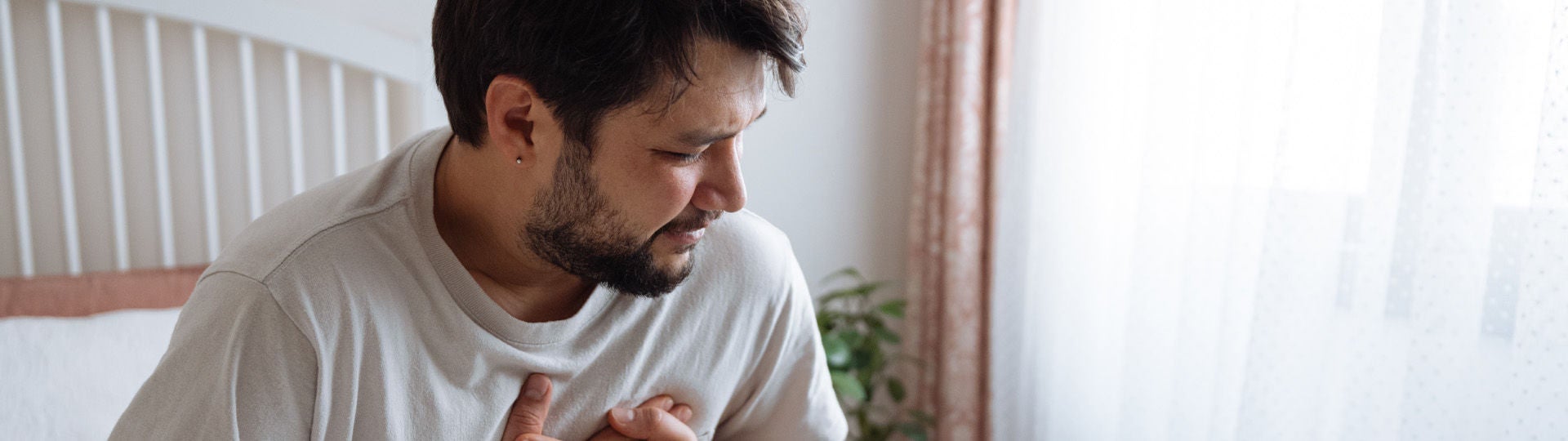 Junger Mann sitzt auf dem Bett und hält sich die schmerzende Brust. Bildquelle: iStock/ozgurcankaya