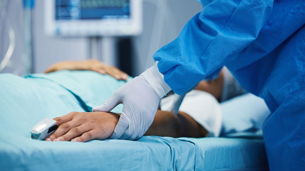 Ein Arzt mit Handschuhen hält den Arm eines Patienten auf der Intensivstation.