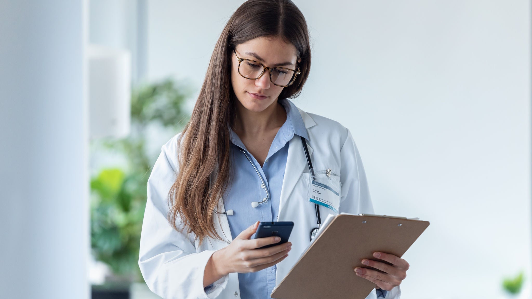Eine Ärztin hält ein Smartphone und ein Clipboard in der Hand