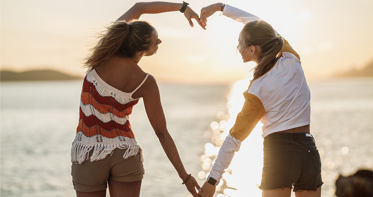 Zwei junge Frauen formen mit ihren Armen gemeinsam ein großes Herz.  Bildquelle: Adobe Stock/milanmarkovic78