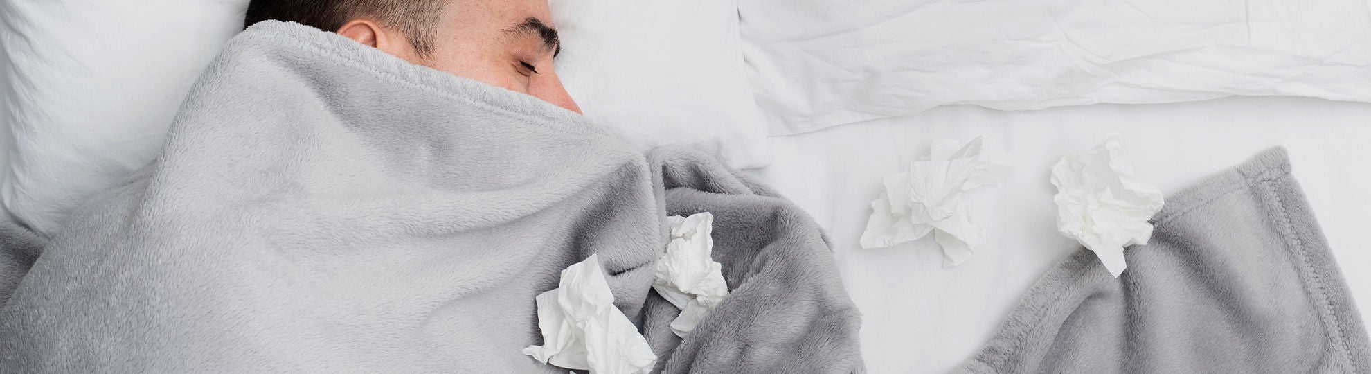Mann liegt umringt von Taschentüchern und offensichtlich krank im Bett. Bildquelle: ©Adobe Stock/nito 