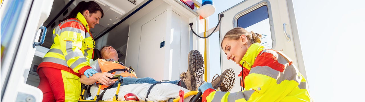 Zwei Rettungssanitäterinnen verladen einen Patienten auf einer Trage in einen Krankenwagen. Bildquelle: iStock/kzenon 