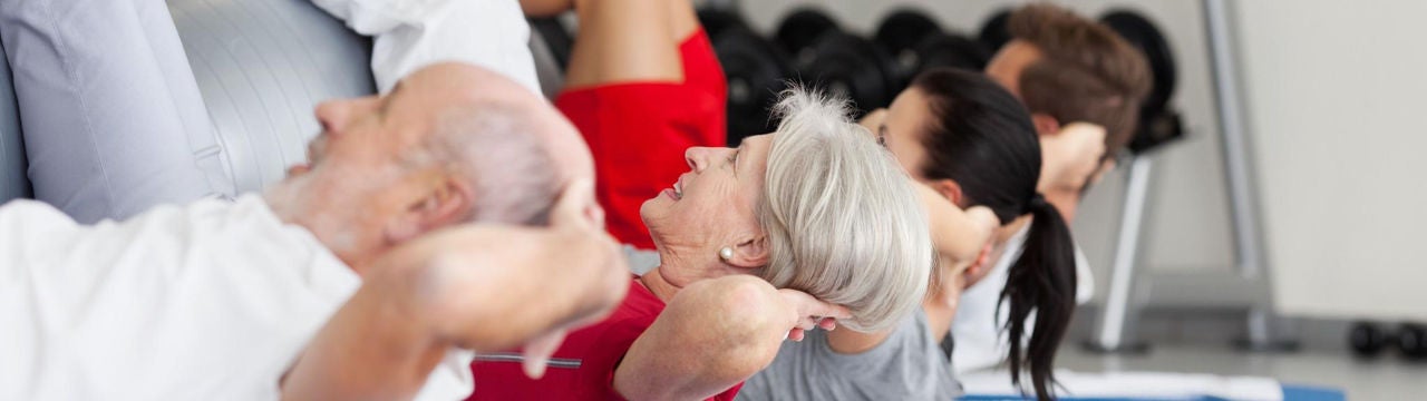 Ältere Menschen machen am Boden in einer Reihe bei der Reha Gymnastikübungen.