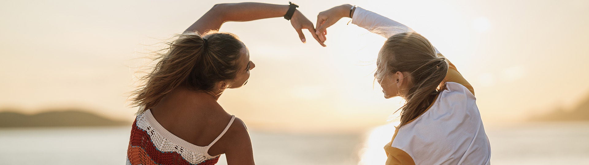 Zwei junge Frauen formen mit ihren Armen gemeinsam ein großes Herz.