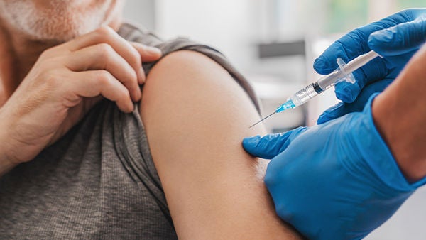 Eine Impfspritze zielt auf einen Oberarm.