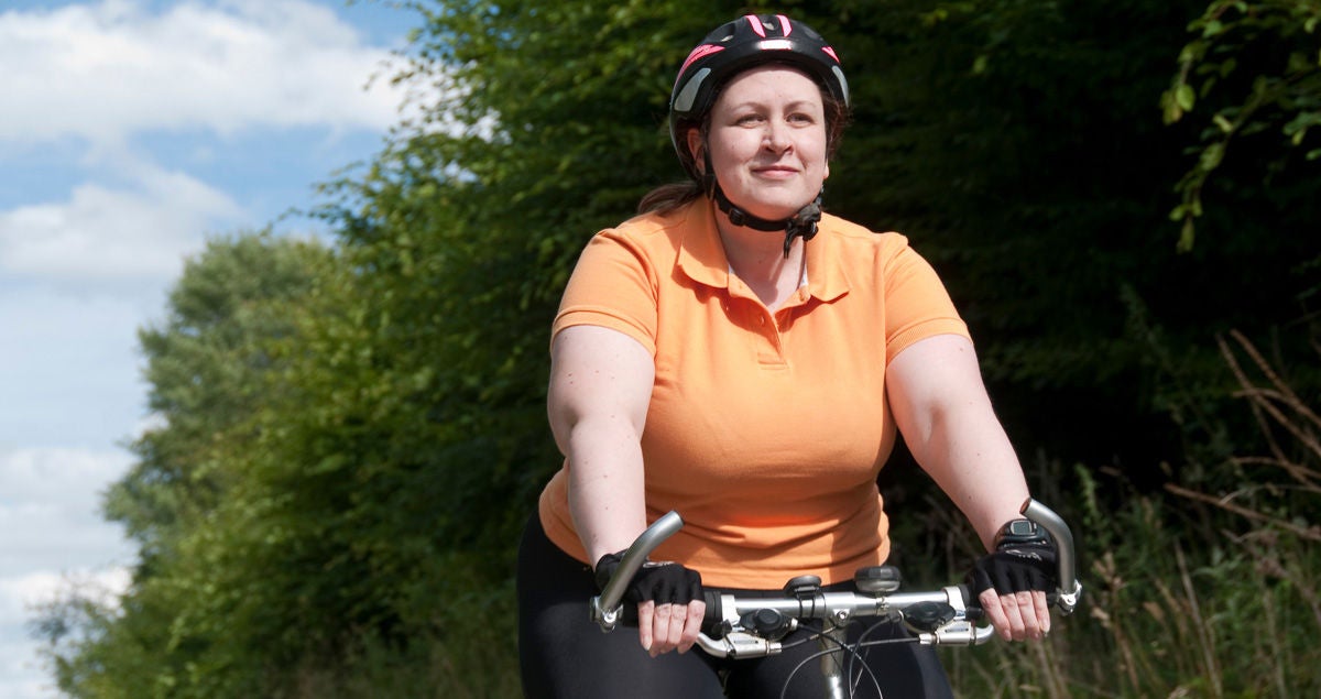 Eine übergewichtige Frau fährt mit ihrem Fahrrad durch die Natur. Bildquelle: Adobe Stock/runzelkorn
