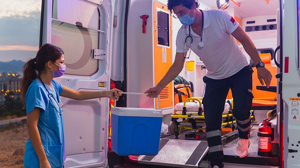 Ein Rettungssanitäter reicht ein Spenderorgan in einer Kühlbox aus einem Rettungswagen an eine Ärztin weiter.