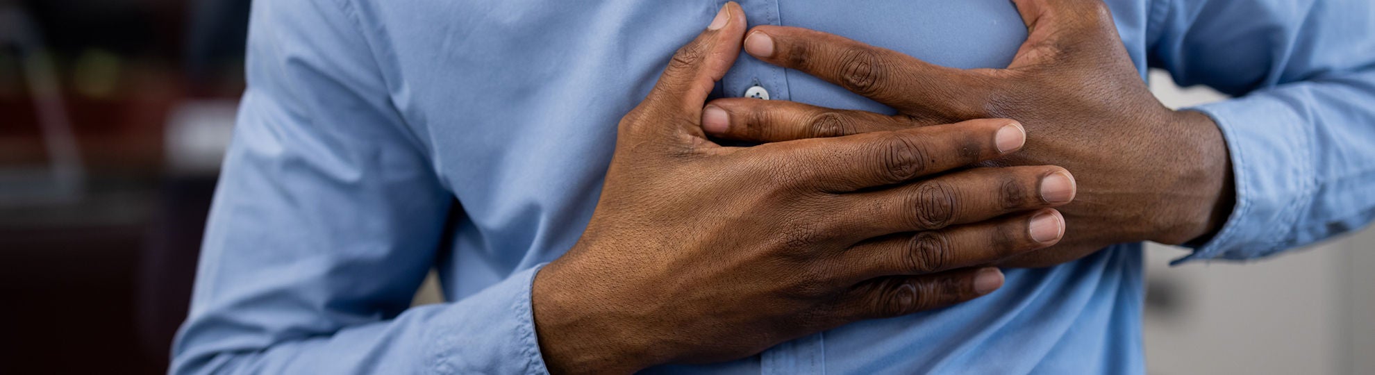 Mann mit Brustschmerzen, der die Brust mit Unbehagen hält und ein blaues Hemd trägt, Bildquelle: ©Adobe Stock/Liubomir