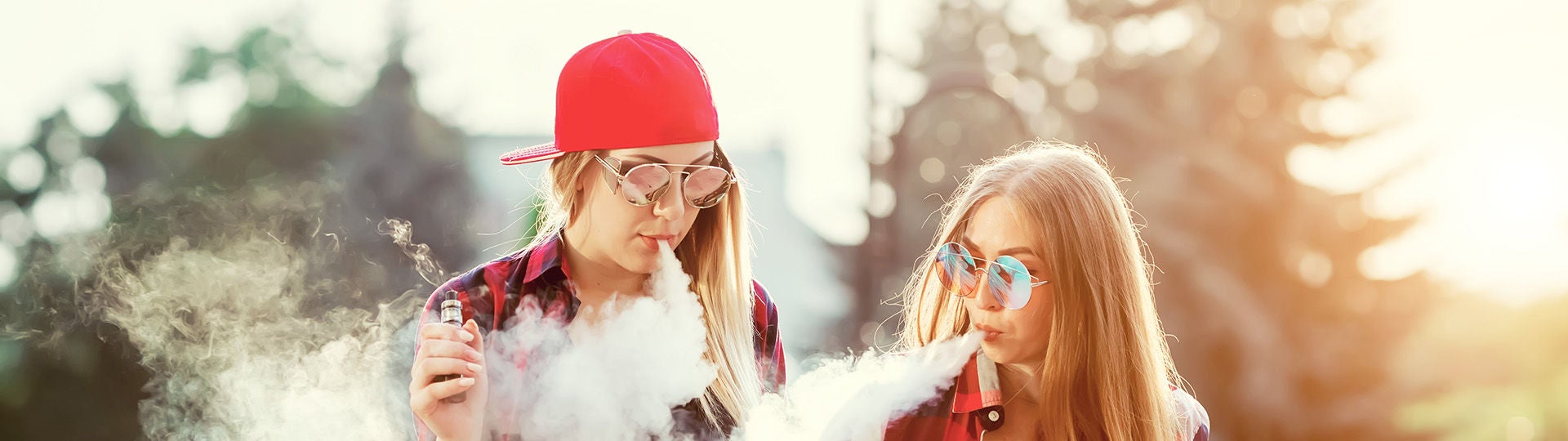 Zwei junge Frauen halten E-Zigaretten in den Händen und inhalieren den Dampf.