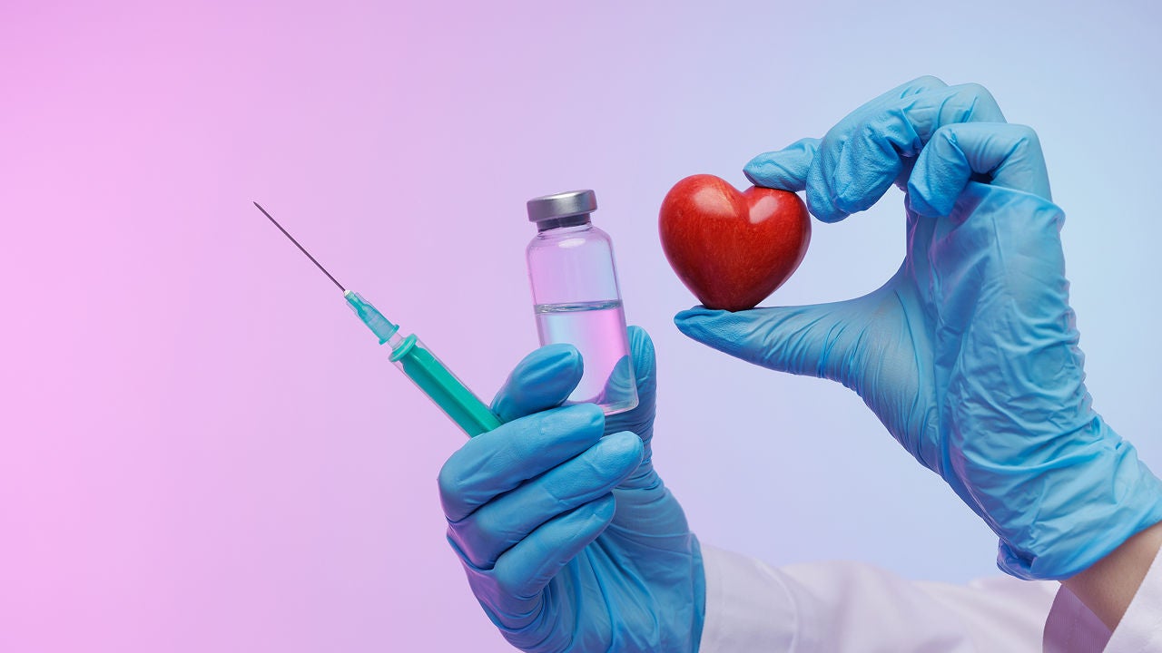 Der Arzt in blauen Handschuhen hält eine Spritze, ein Impfstofffläschchen und ein rotes Herz, das Kardiologie, medizinische Behandlung, Herzgesundheit und lebensrettende Pflege symbolisiert., Bildquelle: ©Adobe Stock/st.kolesnikov