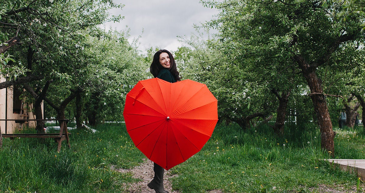 Eine junge Frau steht in einem Park und hält einen herzförmigen Regenschirm in der Hand.