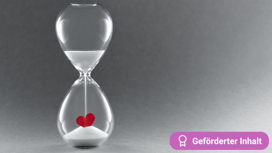 Eine Sanduhr mit rotem Herz vor grauem Hintergrund