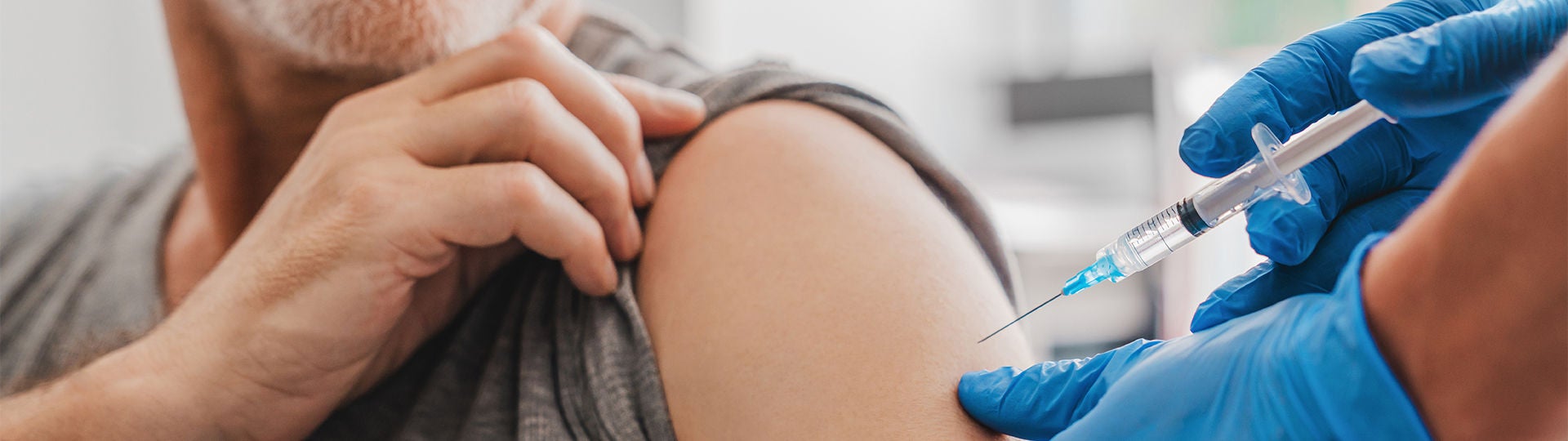 Eine Impfspritze zielt auf einen Oberarm.
