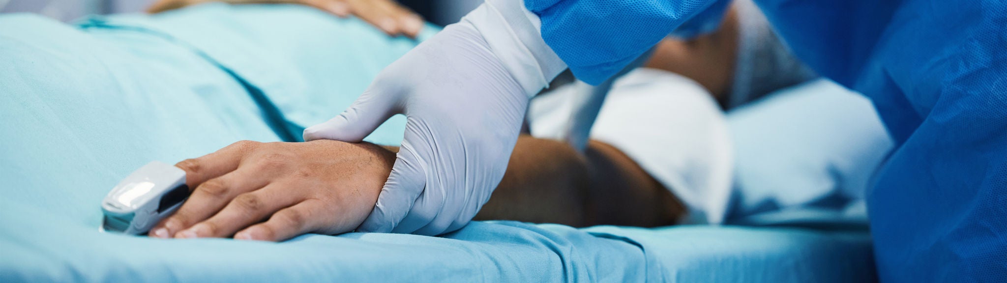 Ein Arzt mit Handschuhen hält den Arm eines Patienten auf der Intensivstation.