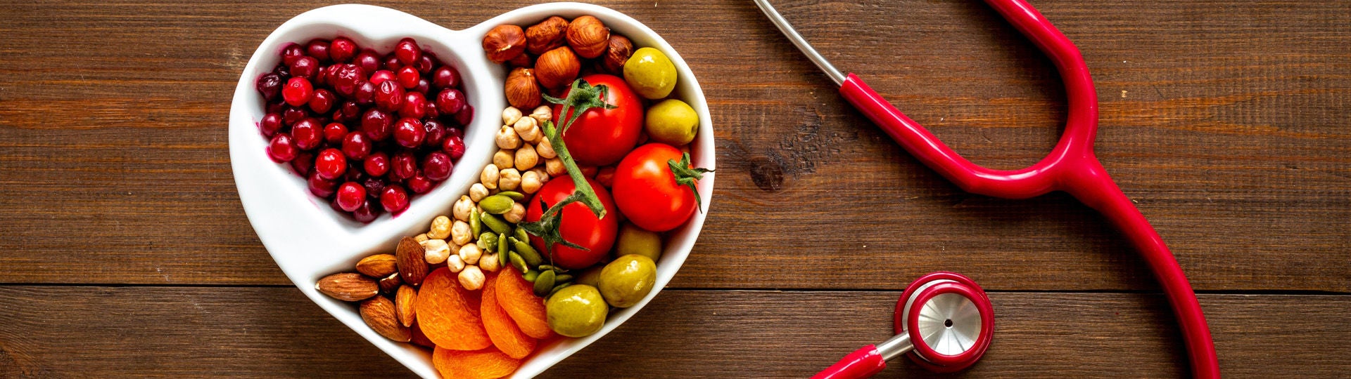 Eine herzförmige Schüssel mit Beeren, Nüssen und Gemüse steht auf einem Tisch, rechts daneben liegt ein Stethoskop. Bildquelle: Shutterstock/9dream studio