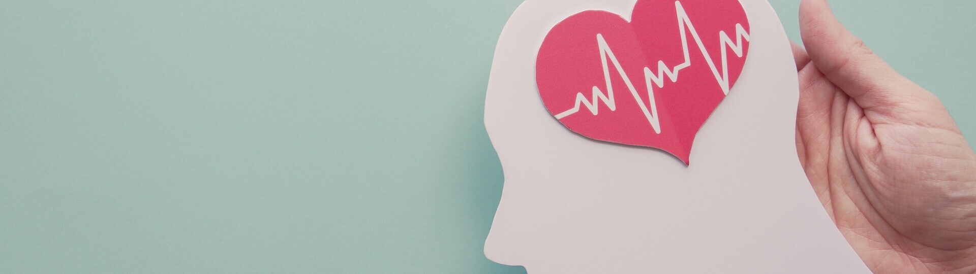 Zwei Hände halten die Figur eines Kopfes, auf dem ein Herz mit EKG-Linien abgebildet ist