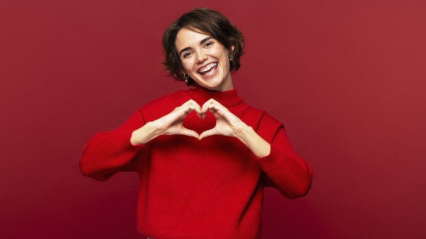 Fröhliche, attraktive Frau, die mit ihren Händen eine Herzgeste macht
