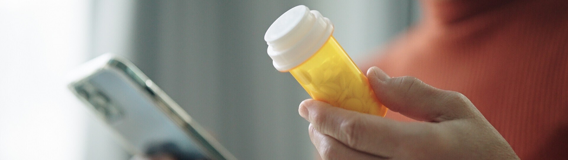 Nahaufnahme der Hand einer älteren Frau, die mit ihrem Smartphone die Informationen auf einer Tablettenflasche prüft.