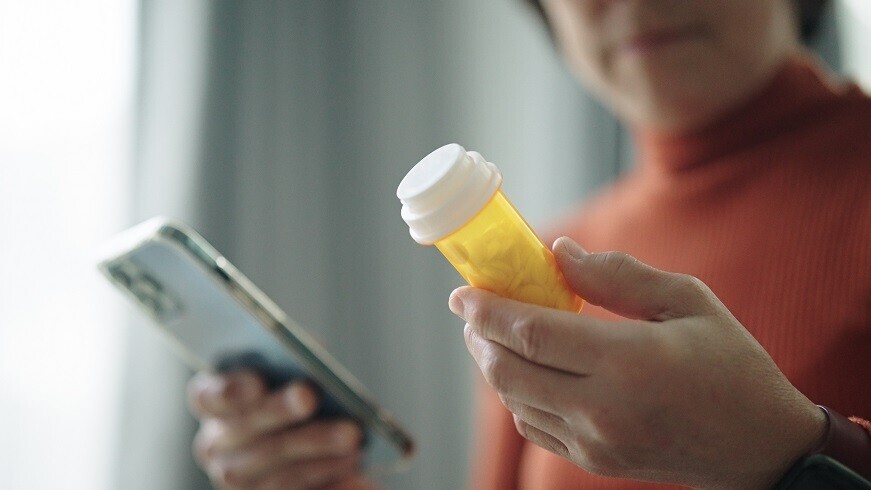 Nahaufnahme der Hand einer älteren Frau, die mit ihrem Smartphone die Informationen auf einer Tablettenflasche prüft.