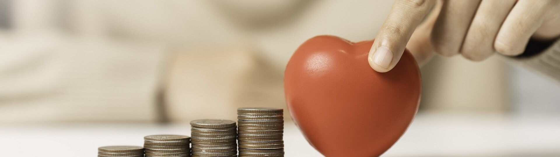 Frau hält rotes Herz und Geldmünzenstapel