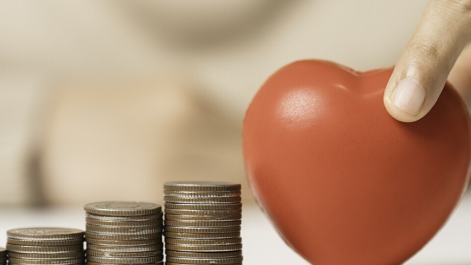 Frau hält rotes Herz und Geldmünzenstapel