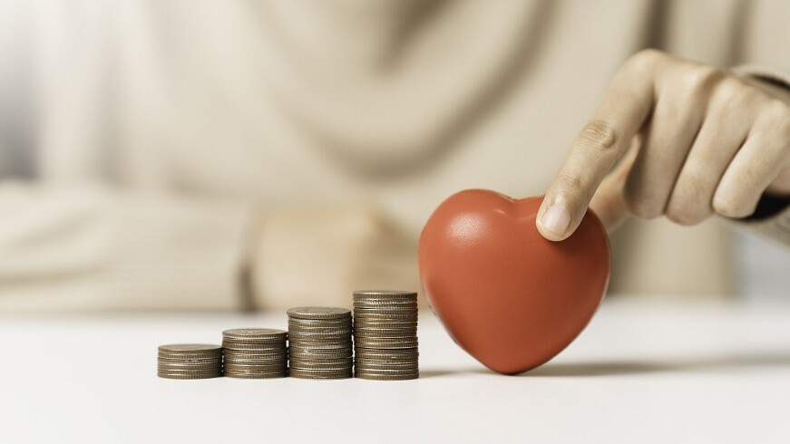 Frau hält rotes Herz und Geldmünzenstapel