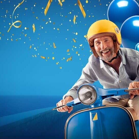 Gut gelaunter Mann sitzt auf einem Mofa mit Ballons