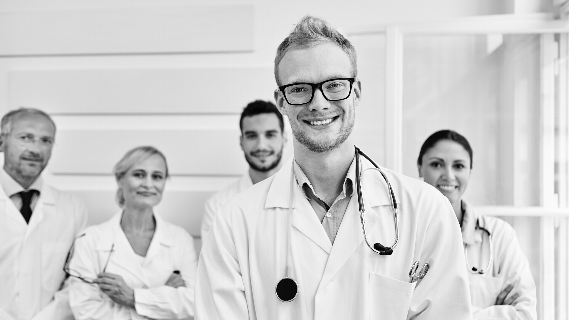 Ärzteteam steht hinter einem jungen Arzt im Krankenhaus