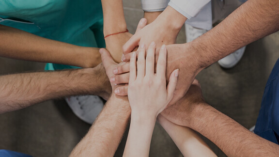 kollegen-halten-haende-zusammen-shutterstock-629115215-1zu1-576x576px-dunkel