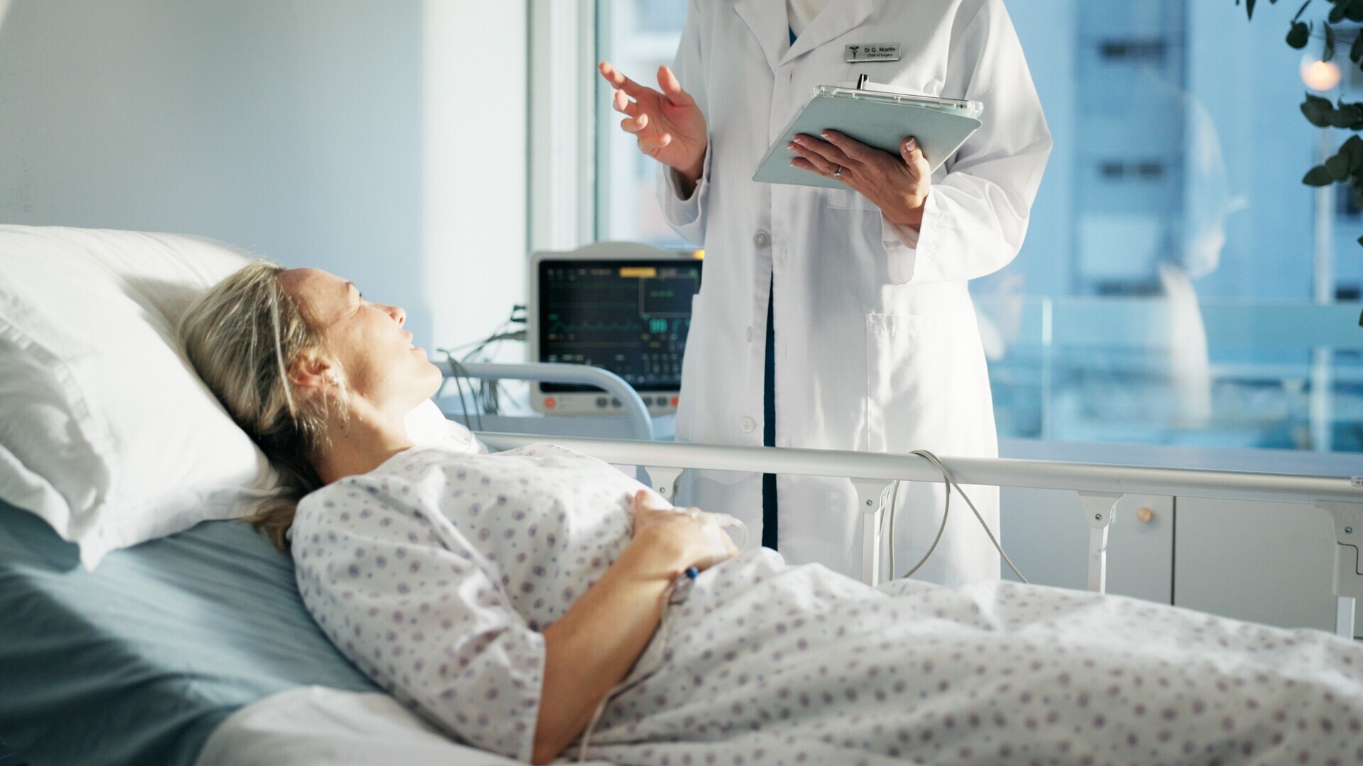 Patientin liegt im Krankenhausbett und unterhält sich mit medizinischen Personal