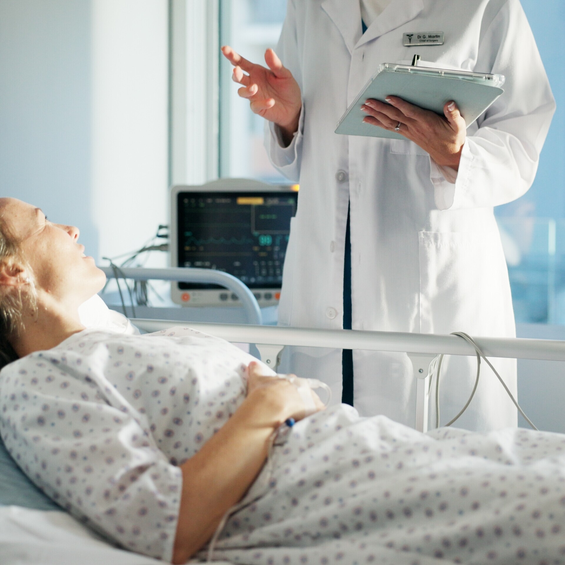 Patientin liegt im Krankenhausbett und unterhält sich mit medizinischen Personal