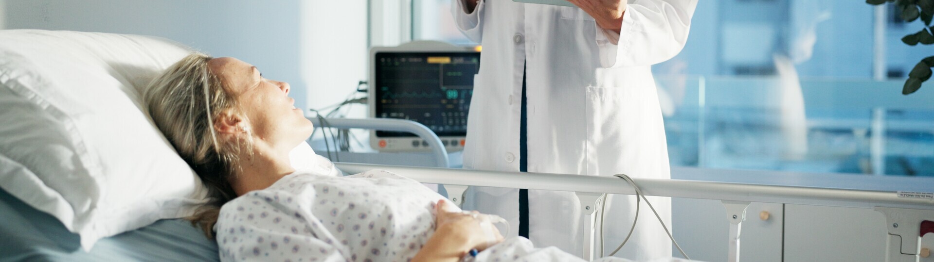 Patientin liegt im Krankenhausbett und unterhält sich mit medizinischen Personal