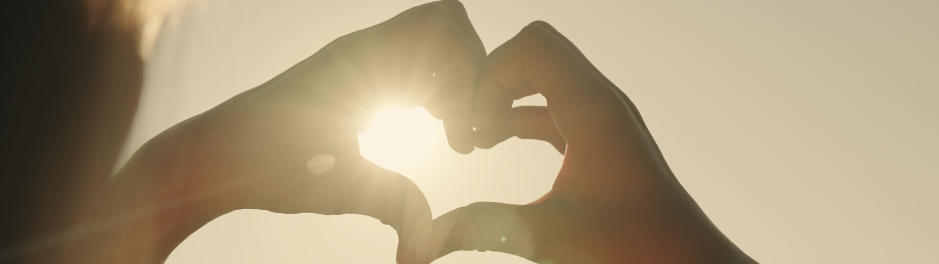Hände formen ein Herz im Sonnenschein